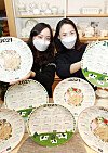 Models pose with dishes showing the 2021 calendar and images of white oxen, made by ceramic company ZEN, at Lotte Department Store’s headquarters in central Seoul on Monday. According to the lunar calendar, 2021 is the year of the white ox, signifying peace and leisure. [YONHAP]