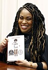 In this Oct. 10, 2018 photograph, author Angie Thomas holds a copy of her novel, 'The Hate U Give,' at a book signing in Jackson, Miss. Thomas' best-selling novel about a black teen murdered by police was adapted into a feature film of the same name. [AP]