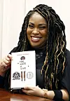 In this Oct. 10, 2018 photograph, author Angie Thomas holds a copy of her novel, 'The Hate U Give,' at a book signing in Jackson, Miss. Thomas' best-selling novel about a black teen murdered by police was adapted into a feature film of the same name. [AP]