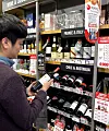 A customer examines a bottle of wine displayed at an Emart24 convenience store. [YONHAP]