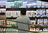 Shopper viewed from behind in front of shelves stocked with milk and other dairy products in Seoul.
