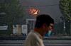 A passerby wearing a mask walks past Kumho Tire’s Gwangju plant in Songjeong-dong, Gwangsan District, as smoke rises from the fire on May 17. [YONHAP]