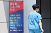 A medical worker enters the emergency center at Seoul National University Hospital in Jongno District, central Seoul, on Friday, passing a banner that notifies the postponement of treatment at the emergency room. [YONHAP]