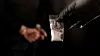 A gloved hand holds a small plastic bag of white powder as a handcuffed individual stands in the background. [JOONGANG ILBO]