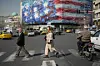 Pedestrians walk past a billboard depicting a U.S. aircraft carrier with damaged fighter jets on its deck and a sign in Farsi and English at Enqelab-e-Eslami Square in Tehran on Feb. 22. [AP/YONHAP]