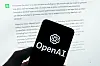 The OpenAI logo is seen on a mobile phone in front of a computer screen displaying output from ChatGPT. [AP/YONHAP]