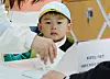 A future voter watches his mother cast her ballot at a polling station at a middle school in Michuhol District in Incheon Wednesday. [YONHAP]
