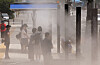 Pedestrians cool off under a shade canopy while walking through a fine spray of cooling mist near Busanjin Station in Dong District, Busan, on June 8, as early summer heat grips the city. [YONHAP]