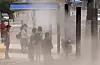 Pedestrians cool off under a shade canopy while walking through a fine spray of cooling mist near Busanjin Station in Dong District, Busan, on June 8, as early summer heat grips the city. [YONHAP]
