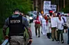 A corrections officer walks beside people holding candles, signs and flowers during a vigil outside the Krome Detention Center in Miami, Florida, United States, on May 24, protesting U.S. Immigration and Customs Enforcement custody and mass deportations. [AFP/YONHAP]