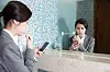 A woman scrolls her phone while brushing her teeth at an office restroom. [GETTY IMAGES]