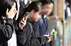 Young students are on their smartphones while waiting to cross a street in Seoul on Nov. 4, 2024. [YONHAP]