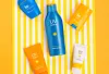 Five colorful Korean sunscreen products arranged on yellow-and-white stripes.