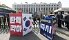 An official from the conservative People Power Party, left, holds up a sign calling for President Yoon Suk Yeol's reinstatement, while a member of the liberal Democratic Party, right, holds up a sign calling for his removal from office in front of the Constitutional Court in Jongno District, central Seoul, on March 23. [NEWS1]