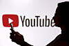 A teenager poses for a photo while holding a smartphone in front of a YouTube logo in this illustration taken Sept. 11. [REUTERS/YONHAP]