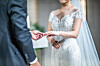 A groom puts a ring on a bride's finger. [SHUTTERSTOCK]