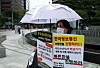 A customer participates in a protest of victims demanding refunds for items bought through credit cards or payment gateways on Qoo10-owned platforms TMON and WeMakePrice. The text reads: 'We demand fast refunds. Credit card companies and payment gateways are shifting the blame. Is it our fault for booking our first-ever vacations?' [YONHAP]
