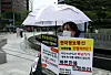 A customer participates in a protest of victims demanding refunds for items bought through credit cards or payment gateways on Qoo10-owned platforms TMON and WeMakePrice. The text reads: 'We demand fast refunds. Credit card companies and payment gateways are shifting the blame. Is it our fault for booking our first-ever vacations?' [YONHAP]