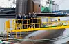 Officials stand on a submarine deck with yellow railings at Hanwha Ocean Shipyard in Geoje, Korea.