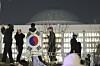A man with the Korean flag draped over his shoulders stands on the wall of the National Assembly in Yeouido, western Seoul, in the early hours of Dec. 4, 2024. [AP/YONHAP]