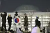 A man with the Korean flag draped over his shoulders stands on the wall of the National Assembly in Yeouido, western Seoul, in the early hours of Dec. 4, 2024. [AP/YONHAP]