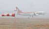 An aircraft lands on the runway at Jeju International Airport while snow falls on Jan. 11, as strong wind and wind shear alerts remain in effect. [YONHAP]
