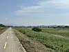 A rural road running past open fields toward distant hills under a partly cloudy sky.