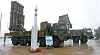 White Cheongung missile displayed beside military launcher vehicles on a wet outdoor lot.