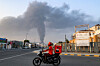 A delivery-person rides a motorcycle along a road as behind a tall smoke plume billows following an explosion in the Fujairah industrial zone on March 3. [AFP/YONHAP]