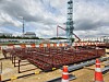 Steel rebar and construction equipment at an outdoor worksite beneath a cloudy sky.