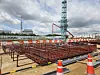 Steel rebar and construction equipment at an outdoor worksite beneath a cloudy sky.