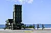 Cheongung-II air defense launcher stands on a coastal roadway with soldiers running nearby.