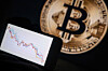 This photograph, taken in Mulhouse on Dec. 5, 2025, shows a phone displaying a downward trend in the stock market in front of a screen displaying a Bitcoin logo. The hype surrounding cryptocurrencies, fueled by the return of U.S. President Donald Trump and the hope of a pro-crypto shift in Washington, seems to have stalled with the brutal fall of bitcoin, highlighting the deep fragility of the sector. [AFP/YONHAP]