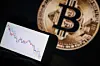 This photograph, taken in Mulhouse on Dec. 5, 2025, shows a phone displaying a downward trend in the stock market in front of a screen displaying a Bitcoin logo. The hype surrounding cryptocurrencies, fueled by the return of U.S. President Donald Trump and the hope of a pro-crypto shift in Washington, seems to have stalled with the brutal fall of bitcoin, highlighting the deep fragility of the sector. [AFP/YONHAP]
