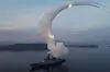 North Korean destroyer launching a missile over calm water with a smoke trail arcing into the sky.