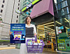 A woman holds up a promotional poster announcing convenience store chain CU's new 24-hour delivery system. [CU]
