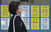 A woman walks by a real estate agency in Seoul with listings displayed on its window on April 16. [YONHAP]
