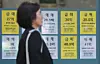 A woman walks by a real estate agency in Seoul with listings displayed on its window on April 16. [YONHAP]