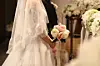 Bride in a white dress and veil holding a bouquet inside a wedding hall.