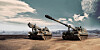 Two K9 self-propelled howitzers sit in a barren field beneath a dramatic sky.