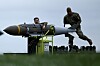 Two USAF personnel prepare a JDAM bomb next to a B-1 Lancer bomber on a runway.