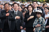 Officials and attendees stand with hands over their hearts during a memorial ceremony outdoors.