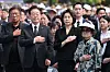 Officials and attendees stand with hands over their hearts during a memorial ceremony outdoors.