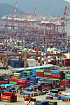 Rows of stacked shipping containers at Busan port with cargo cranes behind them.