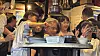 Crowded night market stall with people eating and serving food under bright lights.
