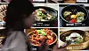 A Seoul restaurant menu board shows photos of various dishes, with a passerby blurred in the foreground.