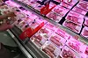 Rows of packaged meat in a refrigerated supermarket display case with red sale signs.