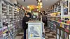 Person browsing in a record store aisle lined with shelves of vinyl records and CDs.