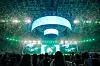 Silhouetted crowd facing a luminous concert stage with a large curved LED screen overhead.