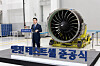 Large turbofan engine displayed on a stage beside a man in a suit at an aerospace event.